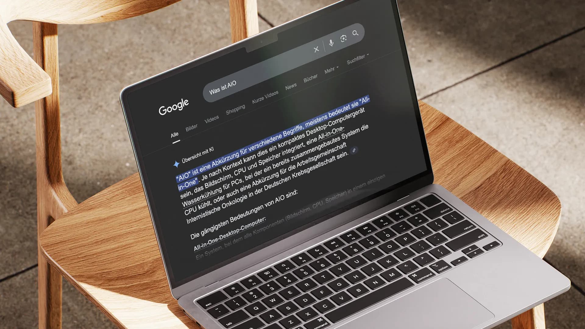 Geöffneter Laptop auf einem Holzstuhl mit Google-Suche nach „Was ist AIO“.